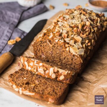 Banana bread loaf on brown crumpled paper with 2 pieces sliced and falling down from the front of the loaf.