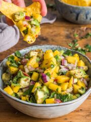 Bowl of mango salsa with some being scooped out on a tortilla crisp.