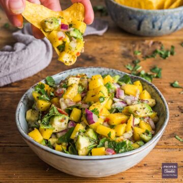 Bowl of mango salsa with some being scooped out on a tortilla crisp.