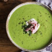 Pea and ham soup in a bowl topped with creme fraiche, chunks of ham and fresh mint