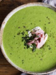 Pea and ham soup in a bowl topped with creme fraiche, chunks of ham and fresh mint