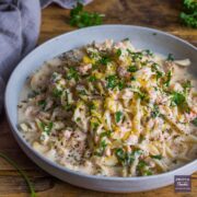 Creamy salmon pasta in a large blue bowl and topped with freshly chopped parsley and lemon zest.