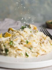 Creamy smoked haddock risotto piled neatly on a small plate, with parmesan being sprinkle on top.