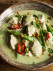 A bowl of Thai green chicken curry with mangetout, green coconut sauce and topped with sliced green chillies and crispy onions.