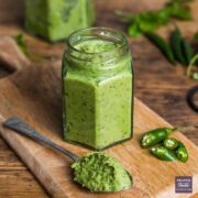 A small jar filled with homemade Thai green curry paste with a spoonful of paste and a chopped up green finger chilli at the side.