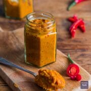 Small jar of Thai red curry paste with a teaspoonful of paste in the foreground.