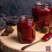 Homemade cranberry sauce in a small jar with a teaspoonful of sauce at the side with larger jar in background.