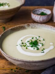 A bowl of leek and potato soup topped with a swirl of cream and chopped chives.