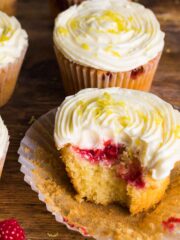 Raspberry muffin topped with lemon butter cream sitting on a muffin case with the sides pulled away and surrounded a few other muffins.