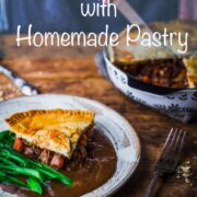 A slice of steak and ale pie on a plate with gravy and tender-stem broccoli with pie dish in the background.