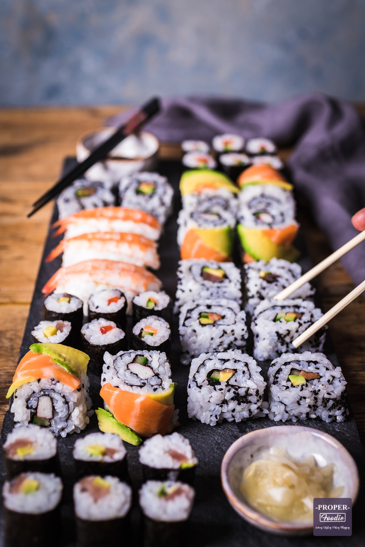 Homemade sushi rolls on a platter with one California roll being picked up with chopsticks