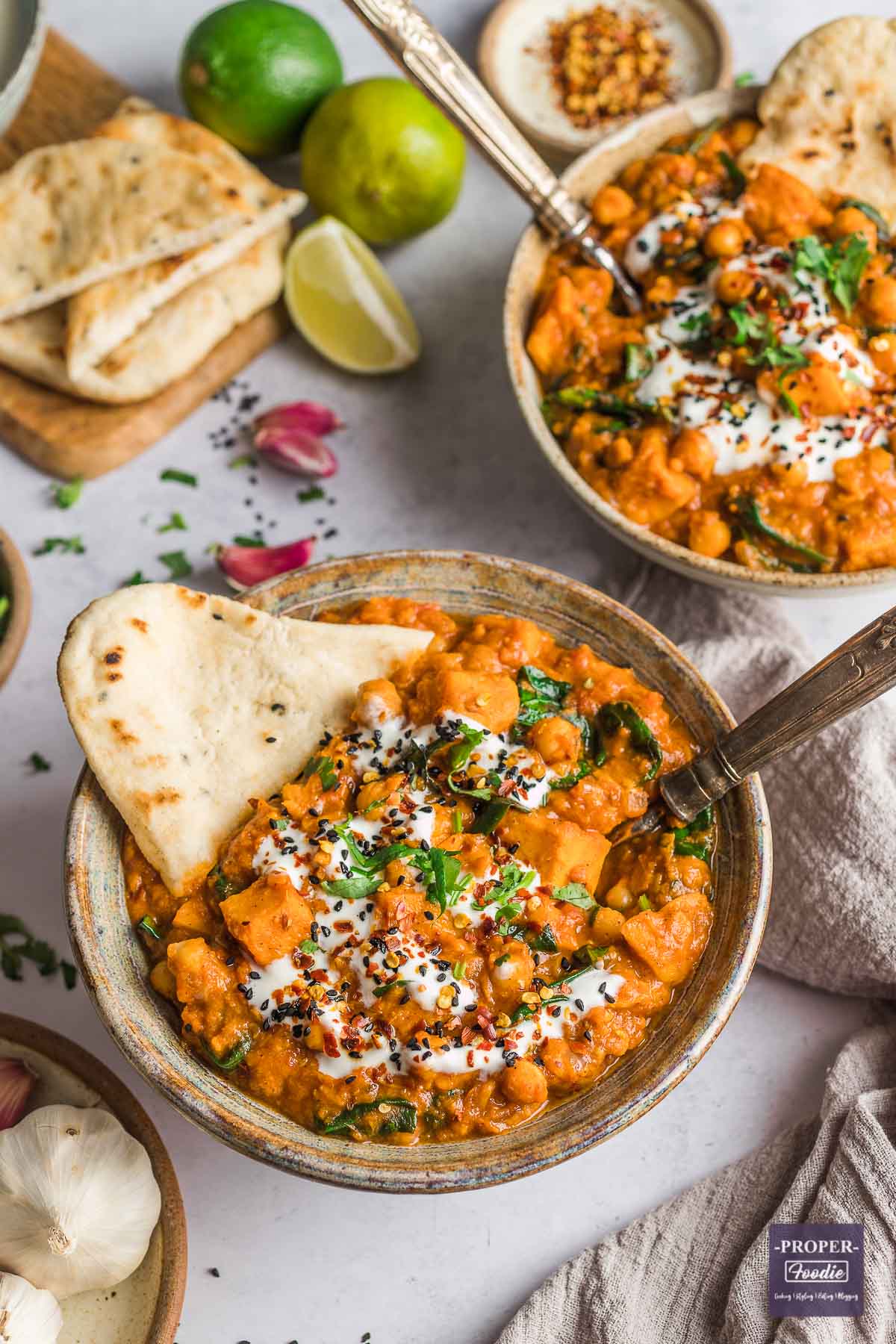 Sweet potato and chickpea curry in a bowl with naan bread and topped with yogurt and coriander.