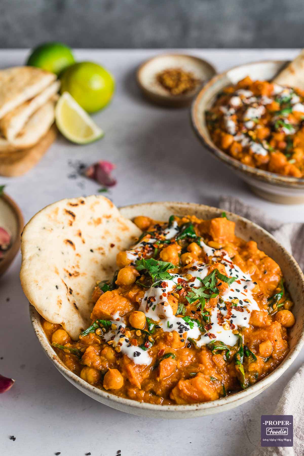 Sweet Potato and chick curry in a bowl with a piece of naan bread and extra naan and lime in the background.