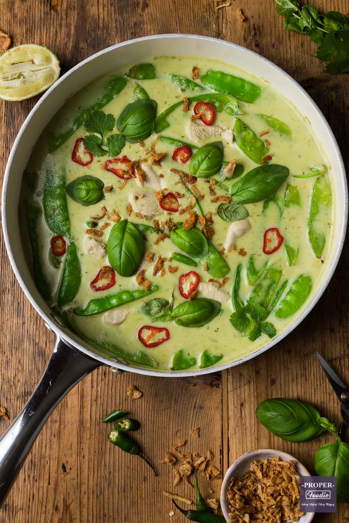 Thai green curry recipe in a large pan topped with sliced red chillies, basil leaves, coriander leaves and crispy onions