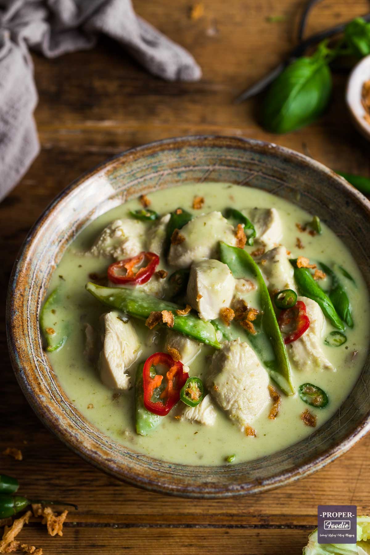 A bowl of Thai green chicken curry with mangetout, green coconut sauce and topped with sliced green chillies and crispy onions.