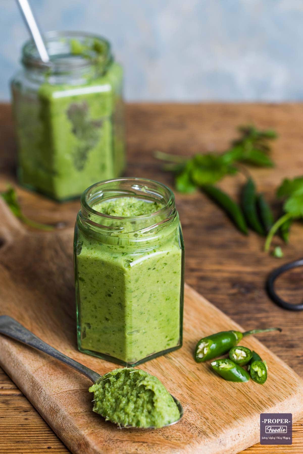 A small jar filled with homemade Thai green curry paste with a spoonful of paste and a chopped up green finger chilli at the side.