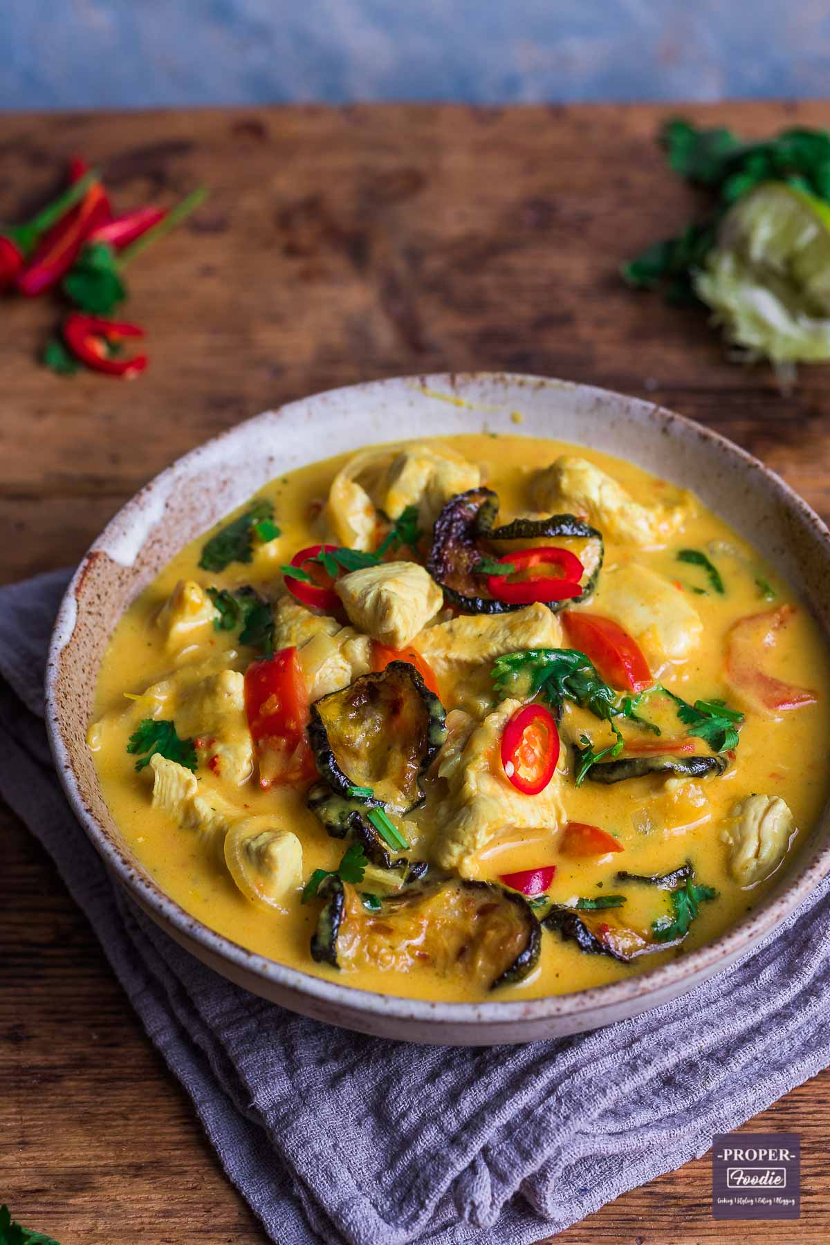 Thai red curry in a large pan with chunks of chicken, roasted courgette and topped with sliced red chilli and fresh coriander.