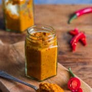 A small jar filled with homemade Thai red curry paste with a spoonful of paste in the foreground and a chopped up red chilli at the side.