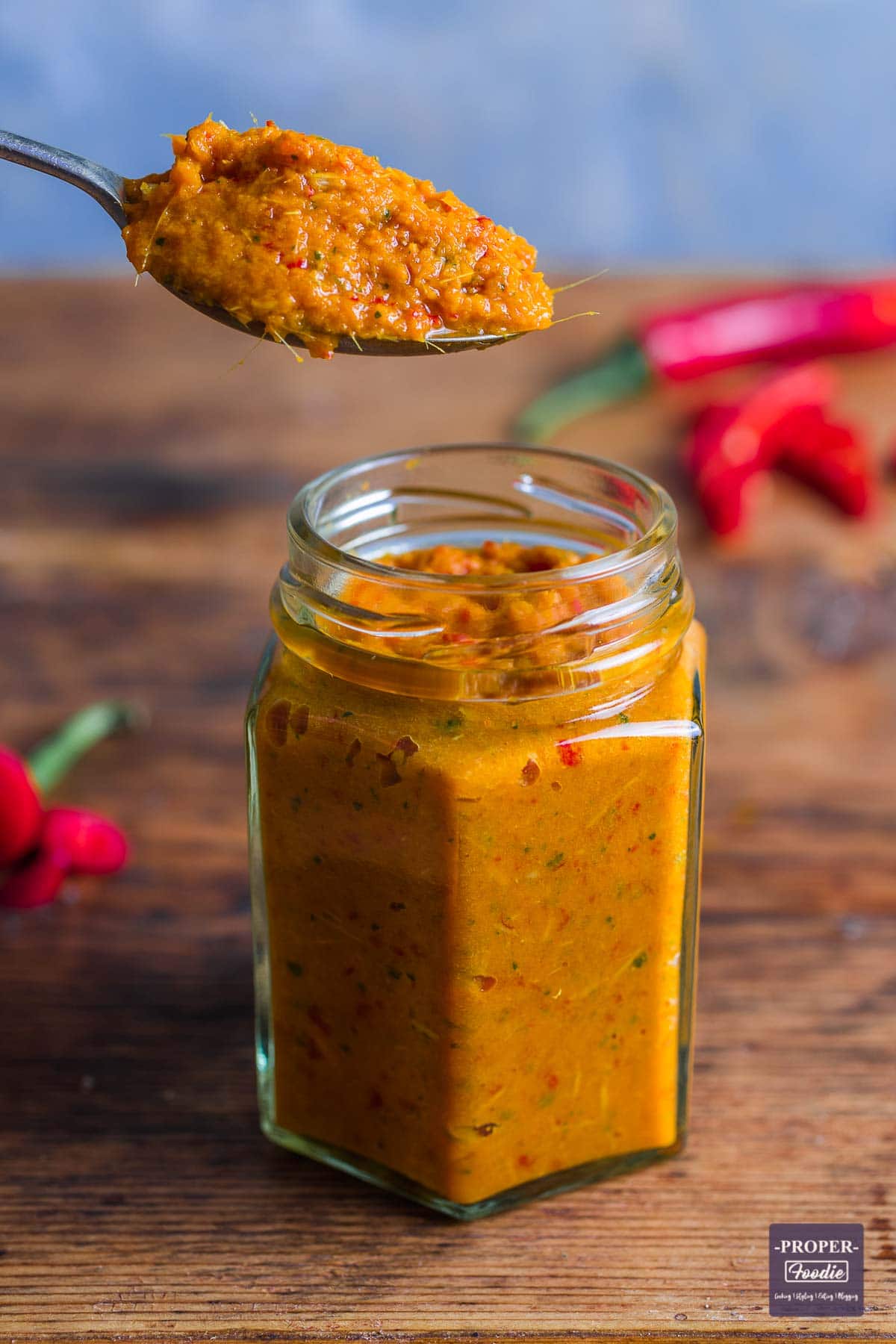 A small jar filled with home Thai red curry paste with teaspoon of paste being held above the jar.