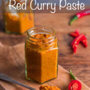 A small jar filled with homemade Thai red curry paste with a spoonful of paste in the foreground and a chopped up red chilli at the side.