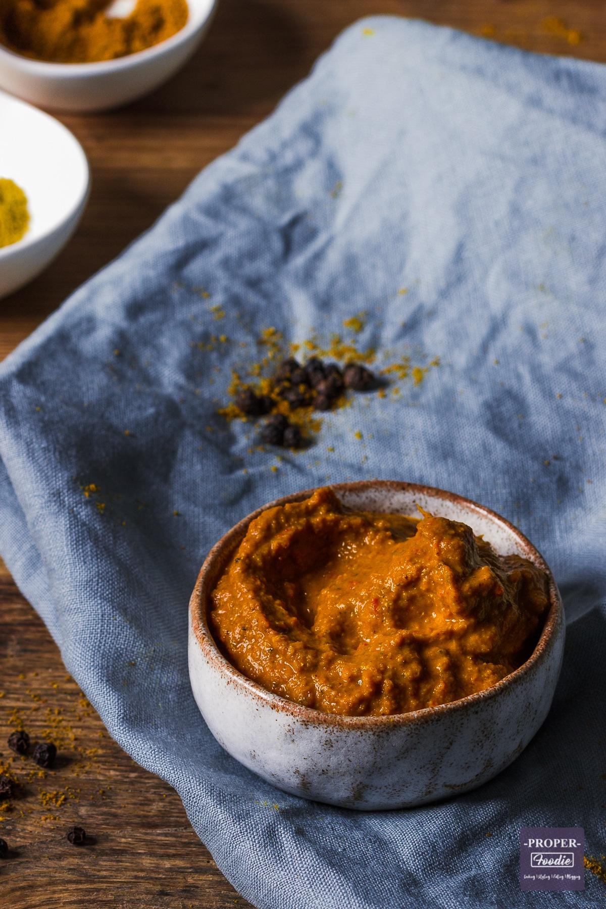 Thai yellow curry paste in a dish with peppercorns in the background