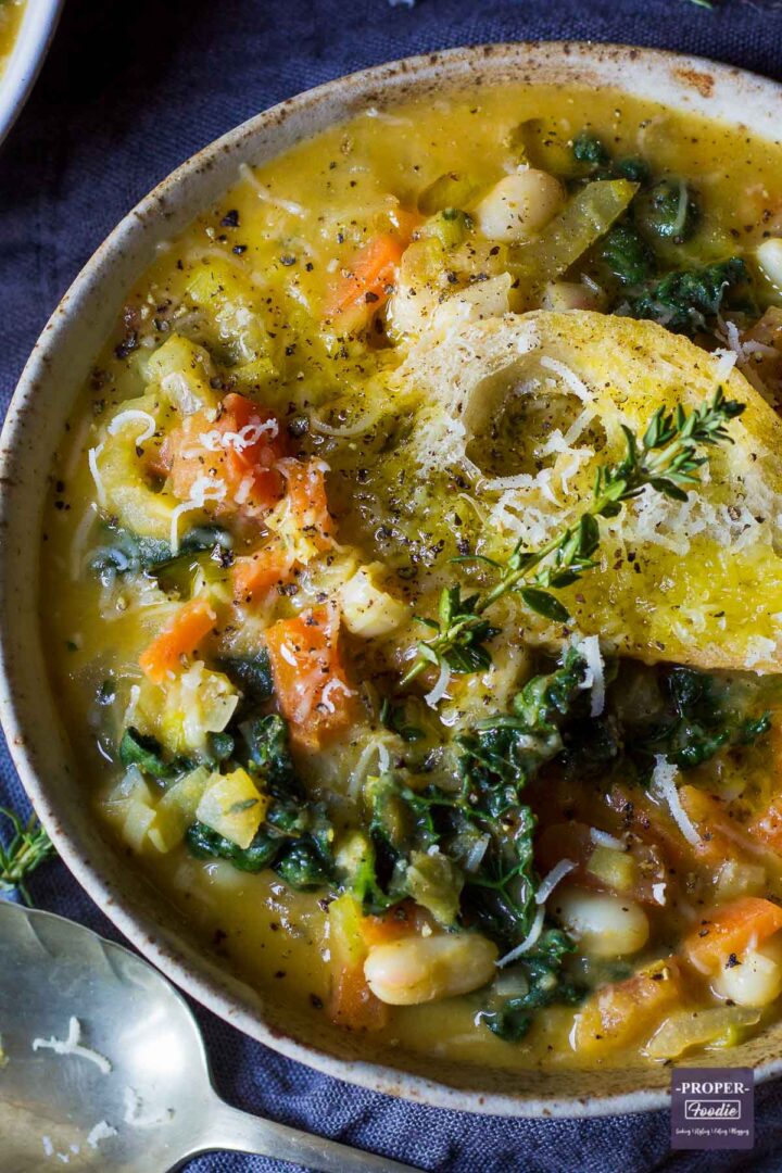 A Tuscan vegetable and bean soup served up a bowl and topped with crusty bread, grated parmesan and fresh sprigs of thyme.