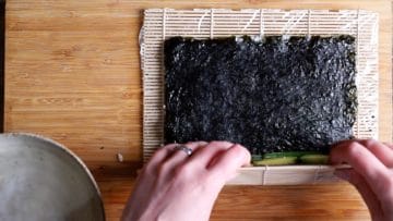 use bamboo mat to start rolling and tightening the sushi roll