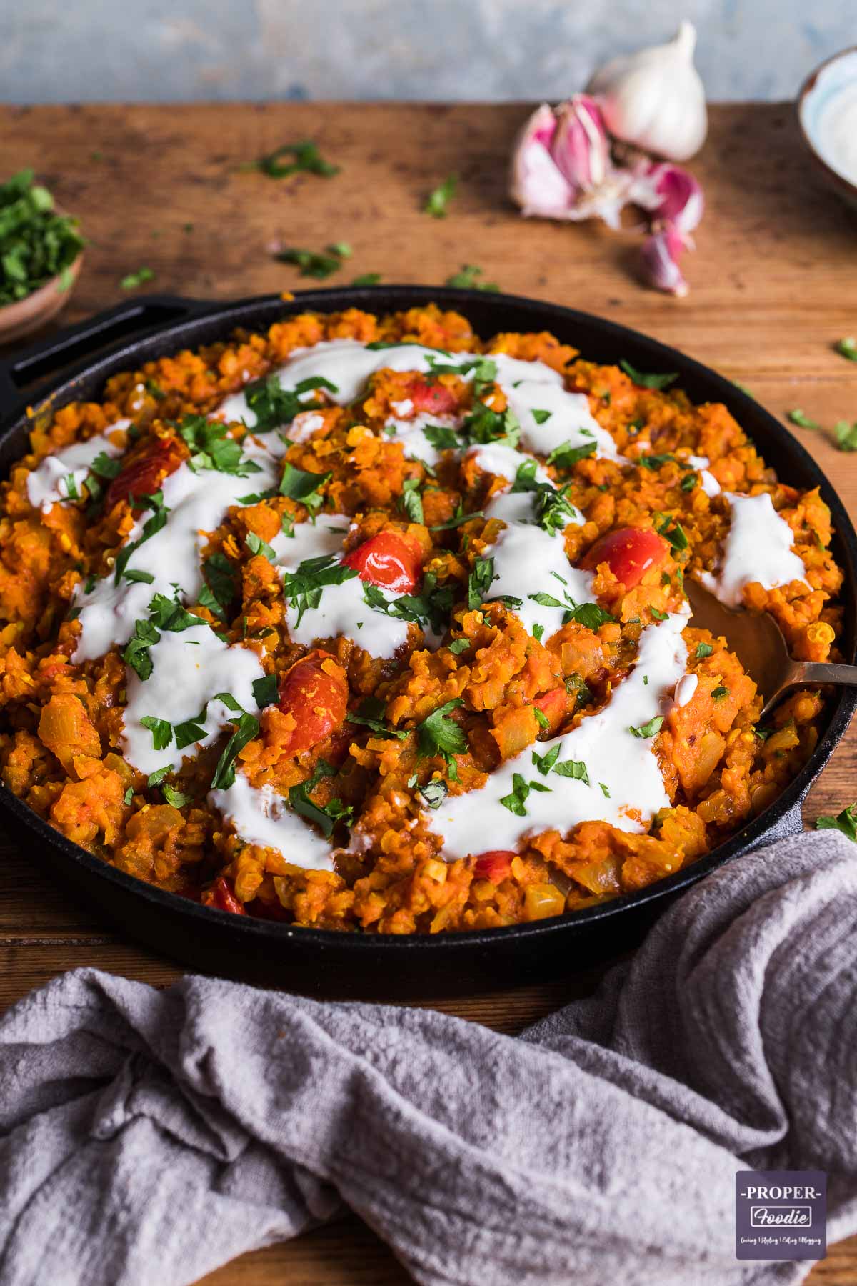 Red lentil dahl in a wide cast iron pan and topped with yogurt and parsley.