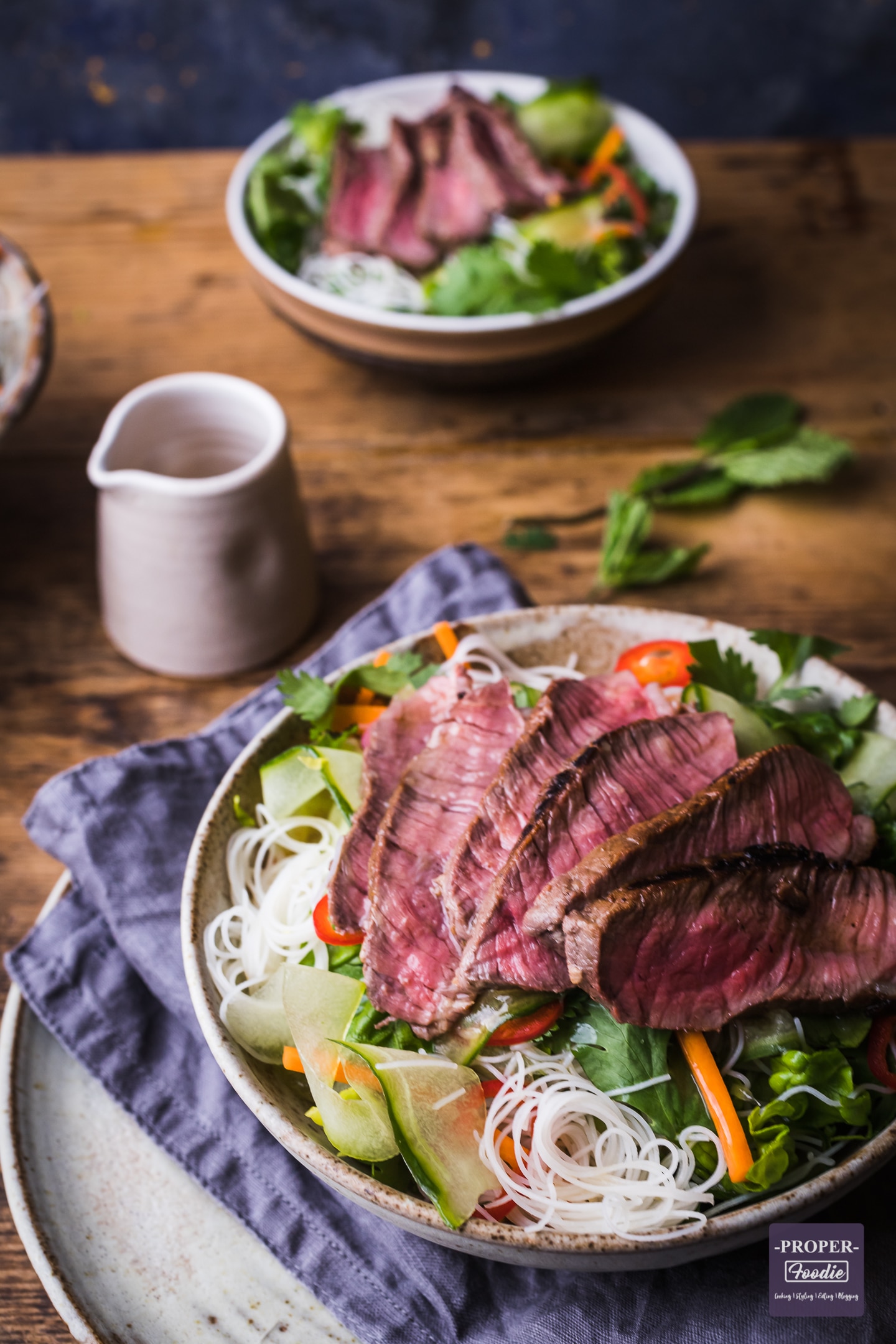 Slices of rare steak over rice noodles and salad in a bowl